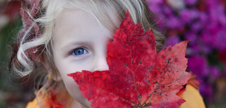 Young girl hiding one eye behind a red leaf