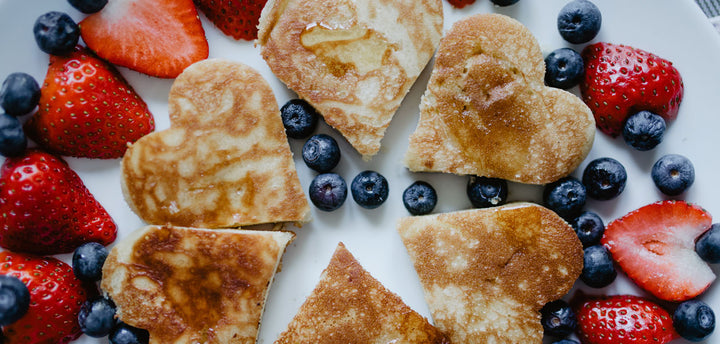 Heart-shaped pancakes surrounded by strawberries and blueberries