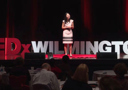 Dr. Julie Wei in a pink dress speaking on the Tedx Wilmington stage