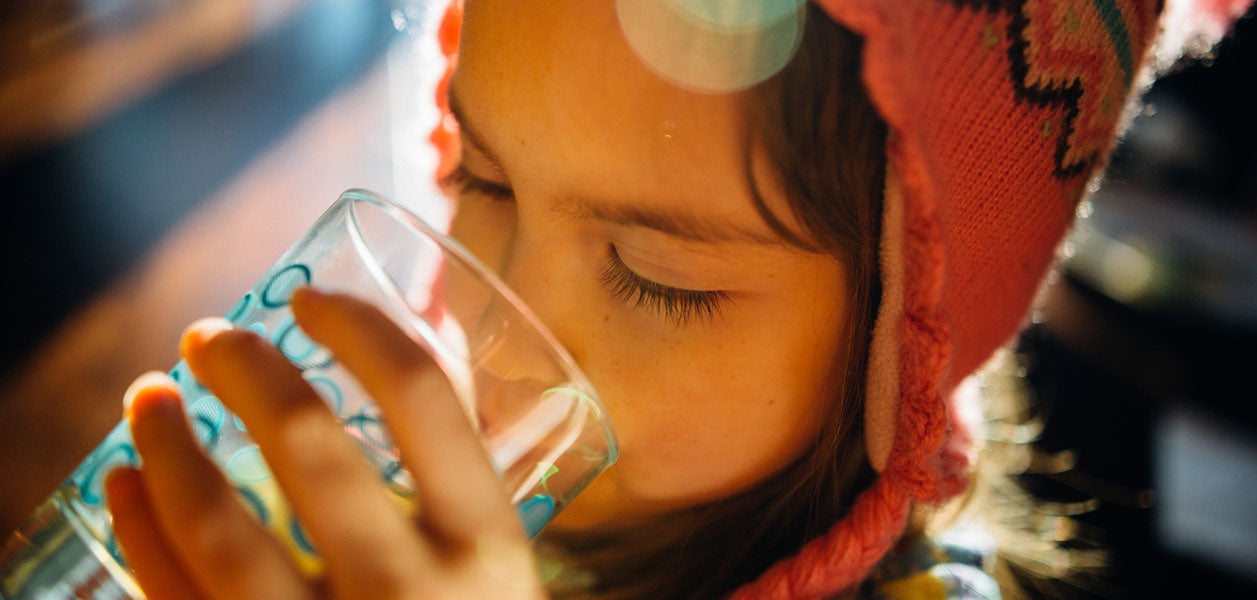 Headshot of a young girl with a beanie on her head drinking from a glass