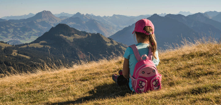 Girl with pink backpack sitting on a mountain