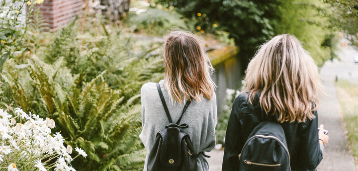 The backs of two female teenagers who are walking down a path