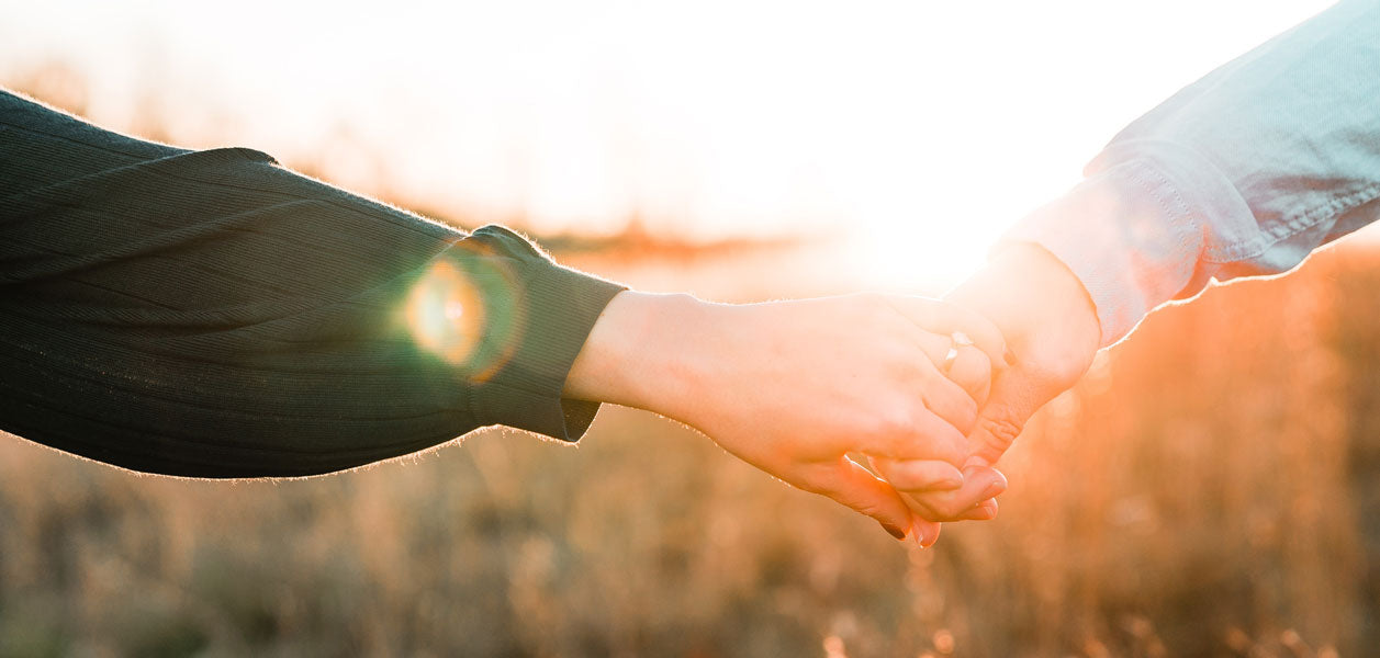Close up of two hands holding each other outside in a field
