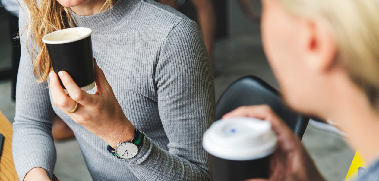 The hands of two blonde women holding disposable coffee cups with lids