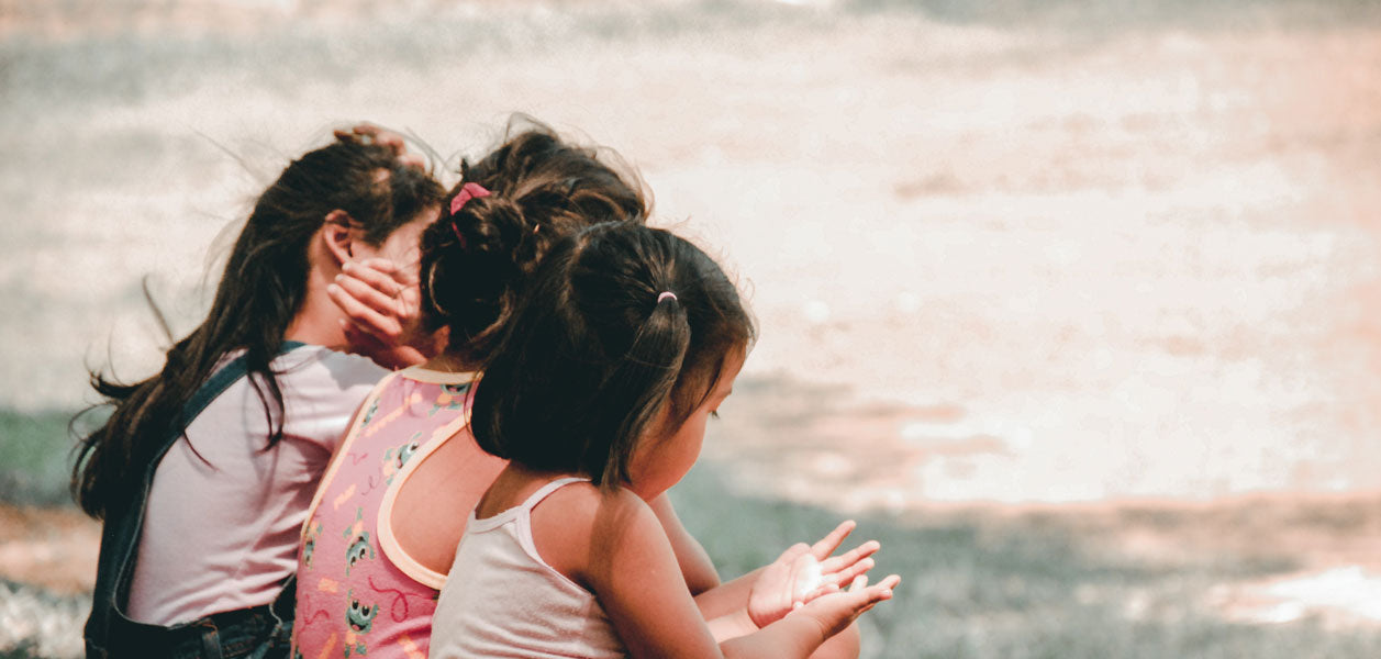 Three dark haired girls sitting outside with their backs to the camera