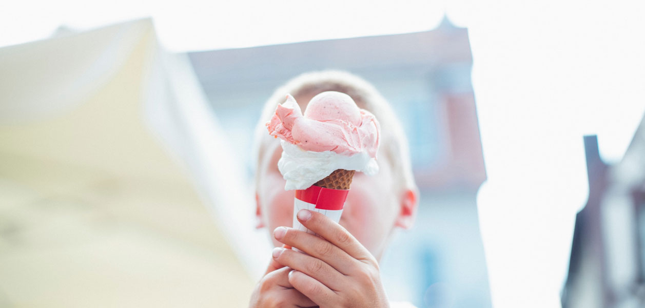 Headshot of a boy holding an ice cream cone in front of his face