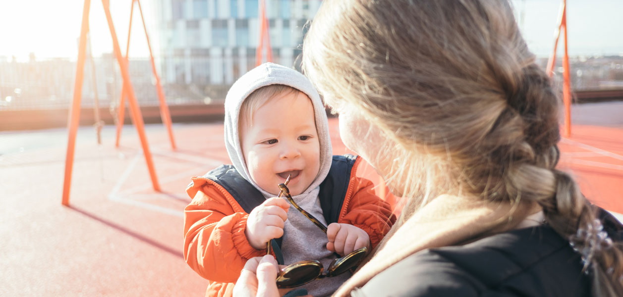 Woman holding a child on a playground who is playing with sunglasses