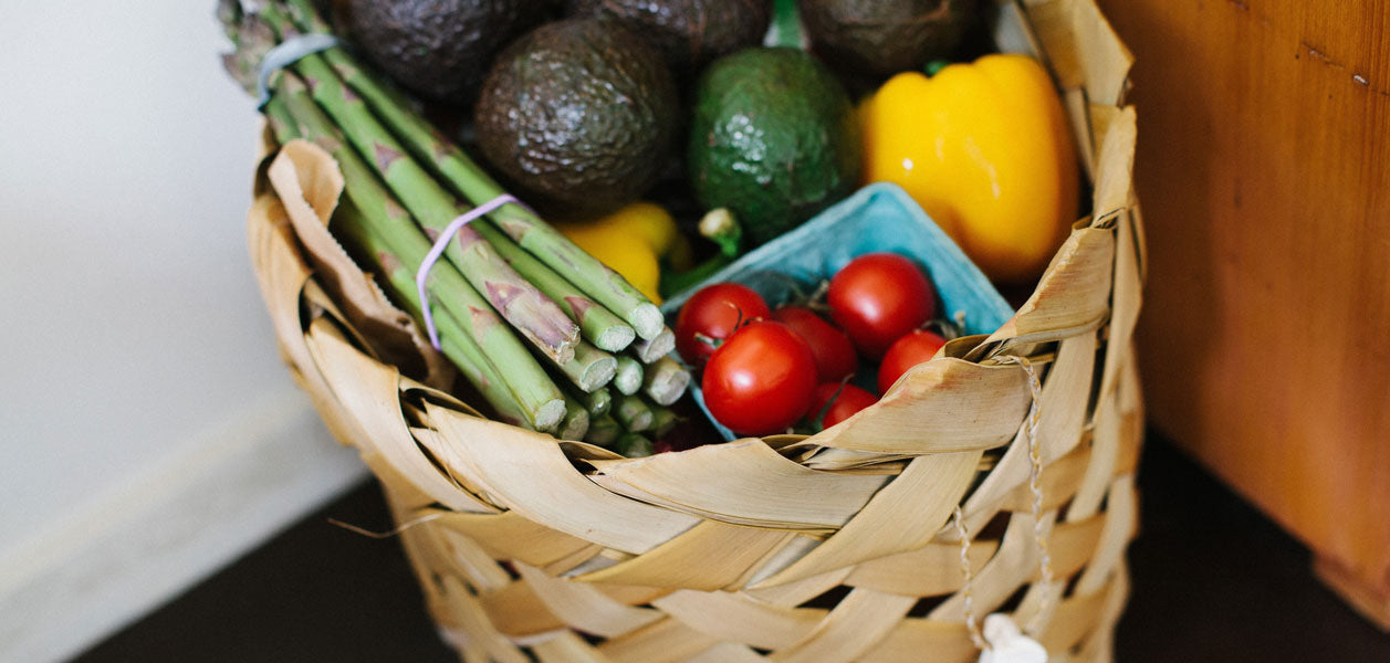 Basket filled with asparagus, avocados, yellow peppers and mini red tomatoes